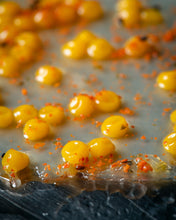 Cargar imagen en el visor de la galería, Perlas amarillas de maracuyá con trozos naranjas sobre fondo gris.