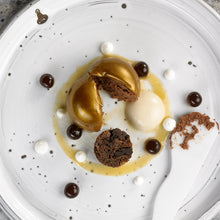 Cargar imagen en el visor de la galería, Postre de chocolate con esfera dorada, crema y trozos de bizcocho en plato blanco.